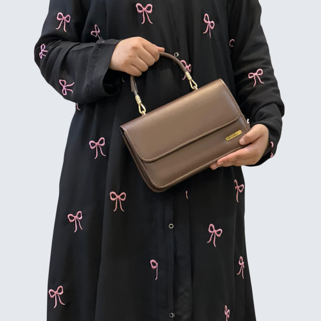 Person holding a brown handbag wearing a black dress with pink bow patterns.