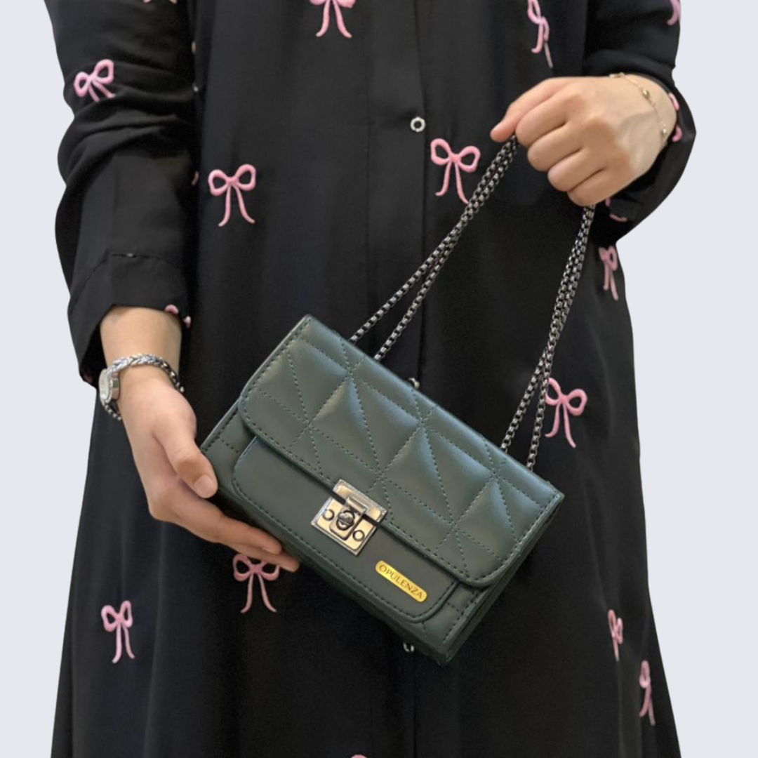 Person holding a green quilted handbag with a black dress featuring pink bows in the background